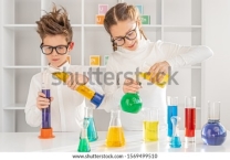 Smart kids in glasses mixing liquids in flasks while doing chemistry experiments in modern laboratory